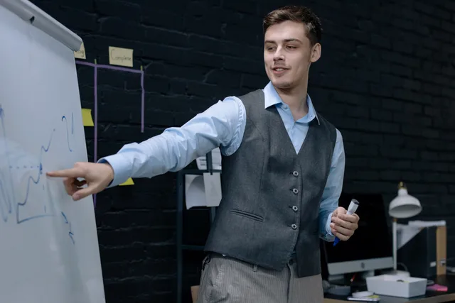 Businessman presenting data on a whiteboard in a contemporary office setting. Berufsbildner und Berufsbildnerin: Qualifikation und Aufgaben im Lehrbetrieb