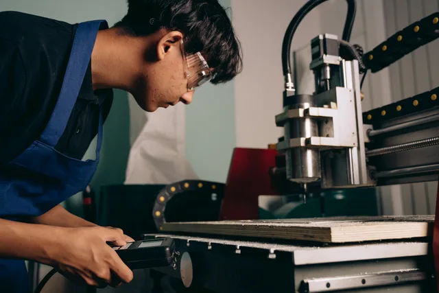 A focused young man wearing safety goggles operates a CNC machine in an industrial workshop. Lernende anstellen: Lohn, Versicherungen und Meldepflichten