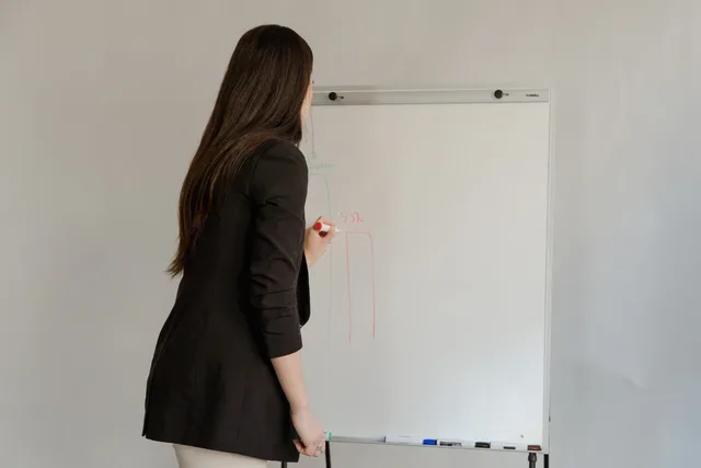 Female employee in black blazer writing on whiteboard during office meeting. Diventare azienda formatrice: requisiti, formazione professionale e vigilanza
