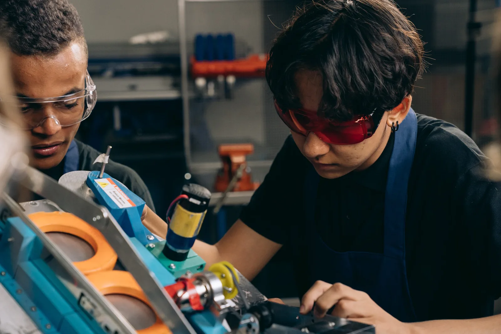 Two young engineers concentrating on precision work in a technical workshop, wearing safety goggles.
